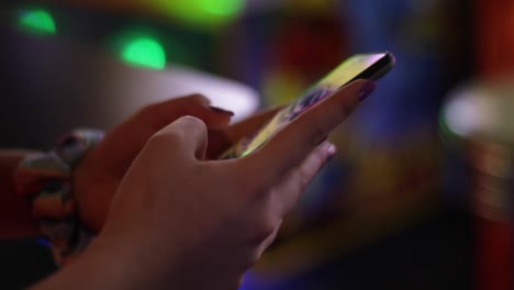 A-young-teenage-girl-holds-her-phone-in-an-arcade-and-types-a-text