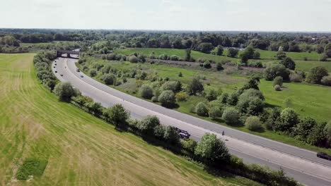 Drone-flying-over-A34-trunk-road-which-is-intersected-by-a-railway-bridge-crossing,-showing-transport-cutting-through-countryside-in-the-UK