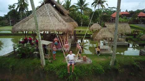 Drone-Shot-of-a-tourist-enjoying-a-swing-between-two-coconut-trees-that-swings-out-over-some-Rice-Terraces-in-Bali,-Indonesia
