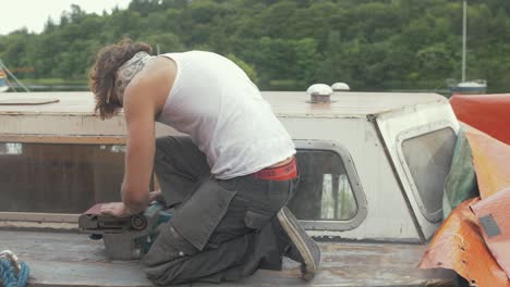 Young-working-topless-in-Summer-sealing-wooden-boat-cabin-roof-to-prevent-leaks
