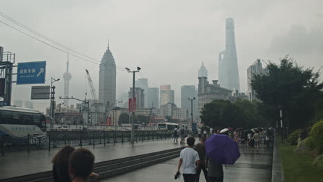 View-of-Shanghai-donwtown-landmark-buildings-from-a-suburb-on-a-rainy,-foggy-day-with-people-passing-by-with-umbrellas,-China