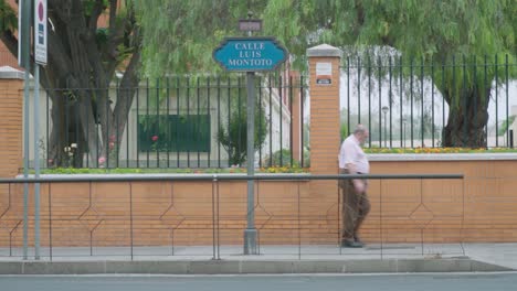 älterer-Mann,-Motorrad-Und-Auto-Passieren-Das-Straßenschild-Luis-Montoto-In-Sevilla,-Slowmo