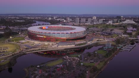 Aerial-view-of-a-Perth's-Optus-Stadium-at-blue-hour-with-gradient-colors-in-the-sky-and-people-walking-towards-the-game,-as-the-camera-moves-to-the-right-and-around-the-stadium