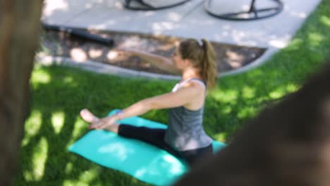 Slow-motion-shot-panning-from-behind-a-tree-and-revealing-a-woman-doing-yoga-on-a-yoga-mat