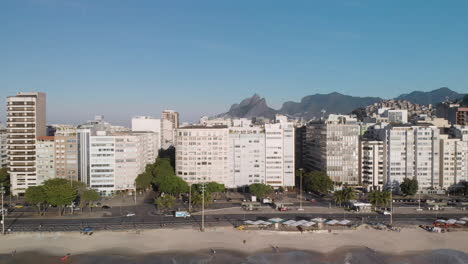 Langsame-Neigung-Aus-Der-Luft-Mit-Den-Zwei-Brüdern-Berg-Und-Ipanema-Im-Hintergrund,-Die-Die-Wellen-Enthüllen,-Die-Am-Copacabana-strand-Hereinrollen,-Und-Die-Architektur-Der-Nachbarschaft-Im-Vordergrund