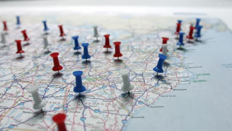 Focus-pulls-onto-red-white-and-blue-pins-placed-marking-cities-on-a-US-map-focused-on-the-East-coast-on-a-map-of-the-USA