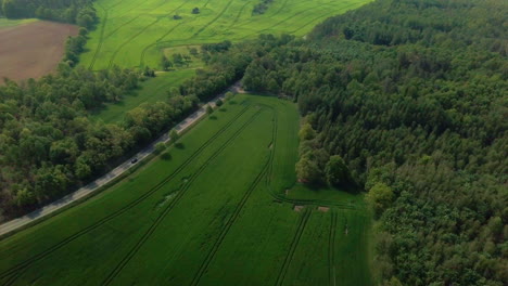 Aerial-view-of-cars-driving-on-a-road-betwenn-fields-and-forest-in-a-rural-area