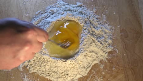 Two-Eggs-Being-Mixed-into-Flour-on-a-Wooden-Work-Surface-for-Baking