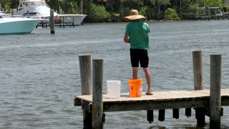 Man-with-hat-and-pole-in-hand-fishing-on-dock---pier-windy-conditions-and-throwing-the-fish-back,-catch-and-release