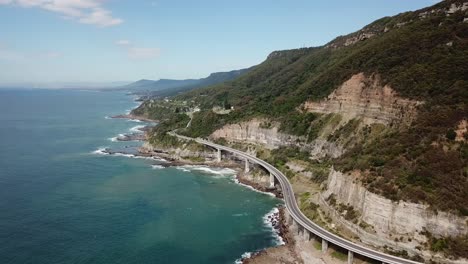Aerial:-High-elevation-drone-shot-tracking-along-side-a-sea-cliff-bridge-as-cars-drive-across-during-a-sunny-day-in-New-south-Wales,-Australia
