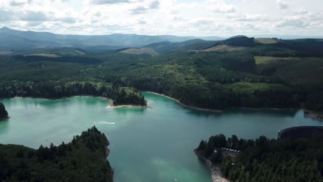 High-up-rotating-aerial-shot-of-a-beautiful-lake-and-dam,-surrounded-by-rich-forests-and-camping-facilities