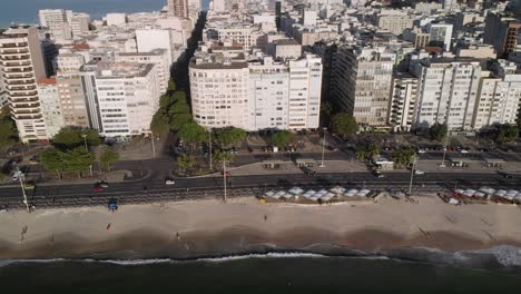 Aerial-slow-descent-showing-Copacabana-beach,-boulevard-and-neighbourhood-seen-from-the-ocean-with-little-movement-in-the-streets-in-the-morning