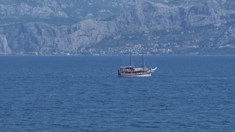 Small-ferry-boat-crosses-middle-of-blue-sea-at-nearby-mountain