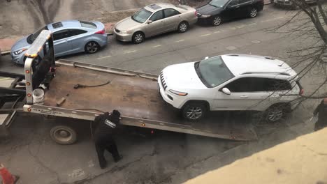 Illegally-parked-car-being-towed-off-of-city-street-with-police-officer-watching