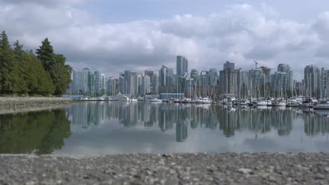 Vista-Panorámica-Del-Centro-De-La-Ciudad-De-Vancouver-En-Canadá-Con-Muchos-Yates-En-El-Puerto-De-Vancouver-vista-Desde-El-Parque-Stanley-Y-Reflejo-De-La-Ciudad-En-La-Superficie-Del-Lago