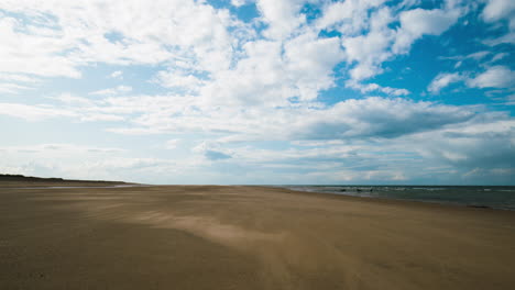 Sand-Weht-über-Einsamen-Strand-Mit-Sich-Bewegenden-Wolken-Darüber