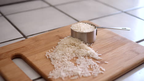 Ein-Haufen-Weißer-Reiskörner-Und-Ein-Messbecher-Für-Zutaten-Auf-Einem-Holzschneidebrett-In-Einer-Küchenrutsche-Rechts