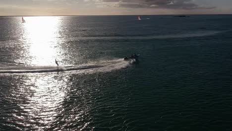 Luftaufnahme-Eines-Wasserskifahrers,-Der-Bei-Sonnenuntergang-Eine-Kurve-Vor-Der-Wasserreflexion-Der-Sonne-Beschreibt