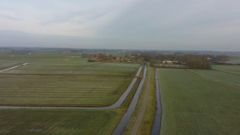 Drone-Pan-hover-flight-Over-meadows-to-a-small-village-in-Europe-The-Netherlands,-Friesland