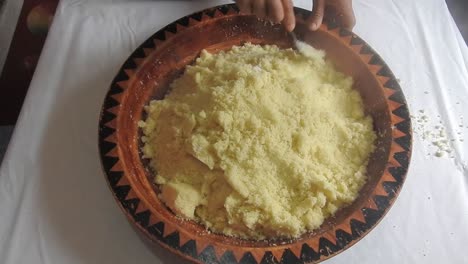 Woman-rolling-hot-semolina-of-couscous-with-spoon-in-a-wooden-dish-at-home-after-steaming-it