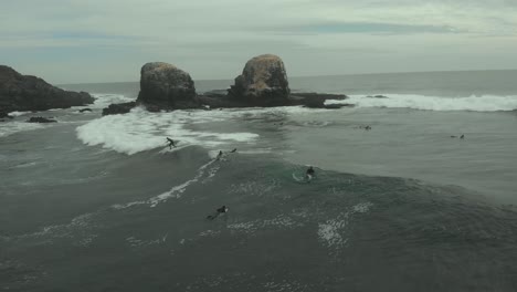 Aerial-of-Pro-Surfer-riding-wave-next-to-Giant-rocks-on-a-cold-cloudy-day,-Pichilemu,-Chile-4K