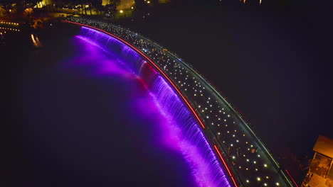 Aerial-view-of-Starlight-Bridge-or-Anh-Sao-Bridge-at-night,-a-pedestrian-bridge-with-strong-colored-lights-and-waterfall-in-District-7-of-Ho-Chi-Minh-City,-Vietnam