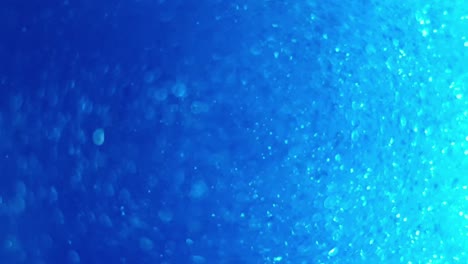 Deep-blue-ocean-color-with-swirling-glitter-and-bubbles-flickering-and-giving-light-pulses-as-they-move,-great-calming-background