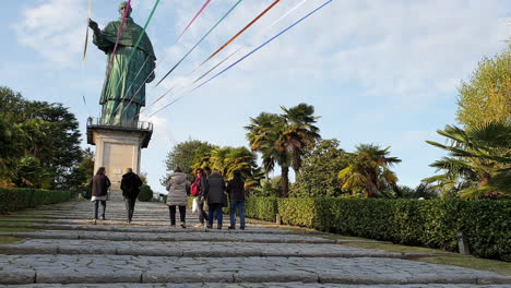 Group-of-tourists-walk-towards-colossus-of-San-Carlo-in-Arona,-Italy