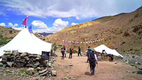 Backpacker-arrives-to-a-camp,-part-of-a-journey-in-the-mountains-of-Himalayas-tents-with-prayer-flags-on-a-sunny-day-on-the-Markha-Valley-trek