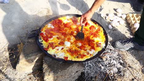 A-man-who-makes-Saffron-tomato-fried-egg-omelet-in-skillet-pan-on-wood-fire-in-nature-outdoor