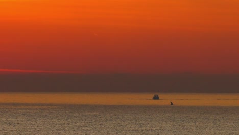 Fishing-Boat-and-kayak-on-calm-sea-under-orange-dawn-sky