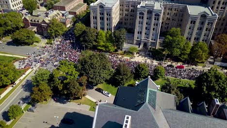Huge-crowd-marches-past-old-buildings-in-Toronto,-aerial-drone-pan