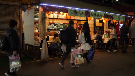 Slow-motion-shot-of-people-sitting-in-a-cafe-and-walking-on-the-Ueno-shopping-street,-at-night-time,-in-Tokyo,-Japan
