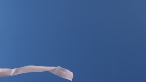 A-toilet-paper-roll-is-seen-flying-through-the-air-slowly-in-front-of-a-blue-backdrop