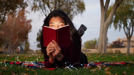 A-young-hispanic-woman-reading-a-book-and-using-her-imagination-to-bring-the-story-to-life-outdoors-in-the-park-at-sunset