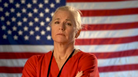 Medium-tight-portrait-of-nurse-looking-extremely-worried-and-sad-with-American-flag-behind-her