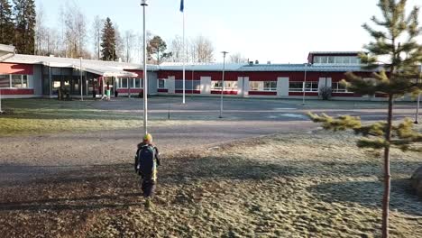 Schoolboy-with-backpack-walking-to-school-in-cold-frosty-weather,-tracking-aerial-shot