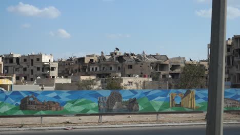 Banner-of-the-top-attractions-in-Syria-displayed-near-the-highway,-ruined-buildings-at-the-back