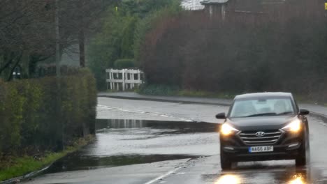 Vehicles-driving-carefully-around-stormy-flash-flooded-road-corner-bend-UK