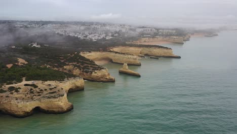 Fontainhas-Galé-Beach-in-the-south-of-Portugal-on-a-foggy-morning-showing-eroded-cliffs,-Aerial-pan-left-shot