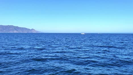 Island-in-the-distance-view-from-the-ocean-with-boat-of-to-the-side-blue-water-and-sky