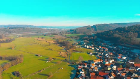 Drohnenflug-über-Einem-Kleinen-Dorf-Mit-See-Im-Hintergrund-An-Einem-Sonnigen-Tag