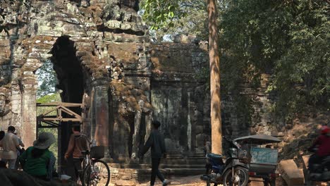 Medium-Exterior-Time-Lapse-of-Ancient-Gate-Leading-to-Angkor-Wat-Temple-With-People-and-Traffic-Going-Through-it-and-Lady-Sitting-With-Her-Back-Towards-The-Camera-in-a-Sun-Hat-in-the-Daytime