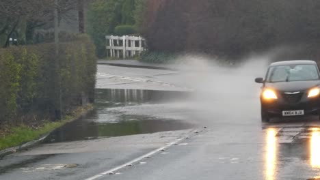 Black-car-splashing-through-stormy-flash-flooded-road-corner-bend-UK