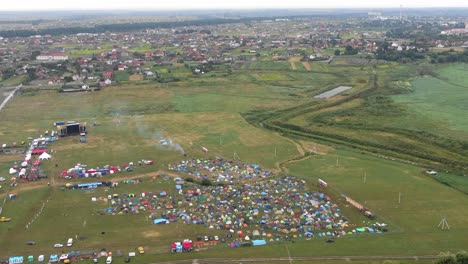 Aerial-View-of-Multi-Colored-Tents-Pitched-in-a-Field-at-a-Music-Festival-With-Town-in-Background