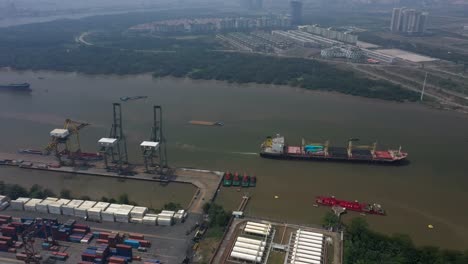 Aerial-view-of-Saigon-River-featuring-the-deep-water-port-facility,-shipping,-wetlands-and-elements-of-the-city-skyline-on-a-day-of-high-air-pollution