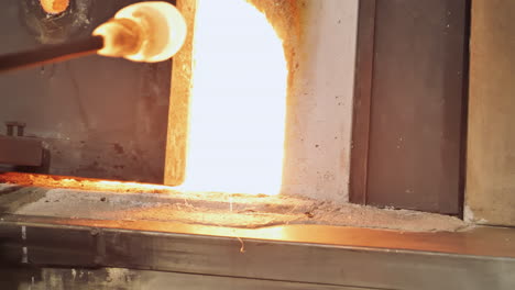 Glass-artist-removes-molten-glass-on-rod-from-white-hot-furnace-in-studio