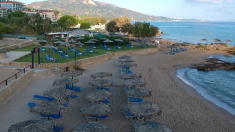 Plaka-beach-resort-shore-on-the-eastern-part-of-the-island-with-chairs,-umbrellas-and-a-volleyball-net,-Aerial-drone-dolly-in-shot