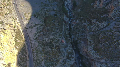Aerial-drone-shot-of-the-rocky-mountains-and-roadway-around-the-Preveli-Beach-during-the-day-time