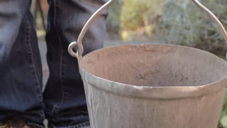 Lady-picking-up-metal-bucket-on-garden-pathway-close-up